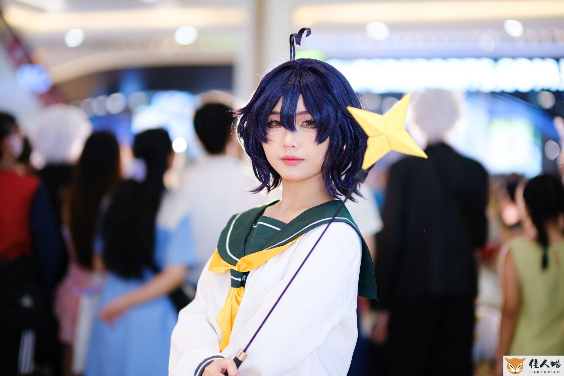 Cosplayer dressed as anime character with a star wand at a bustling indoor event.
