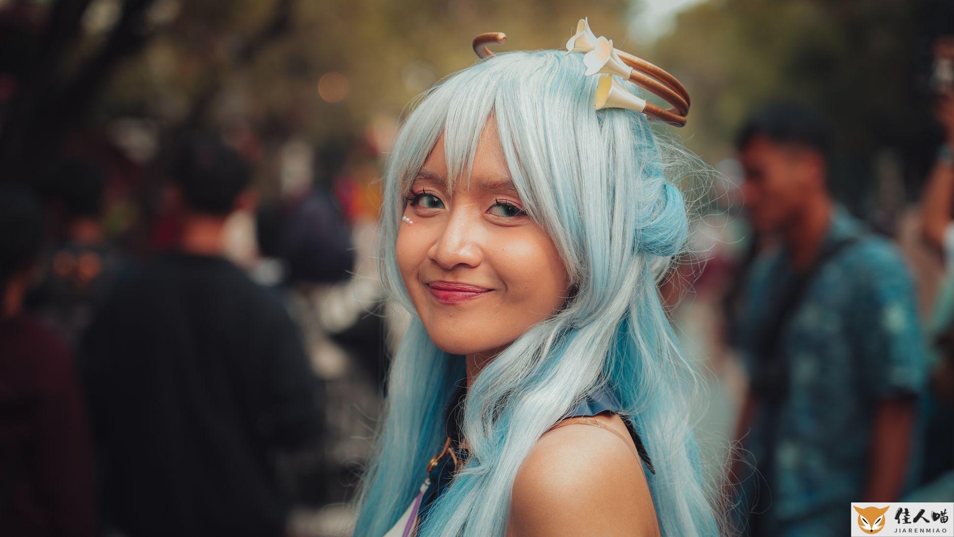 A woman in blue cosplay attire smiles at an outdoor event.