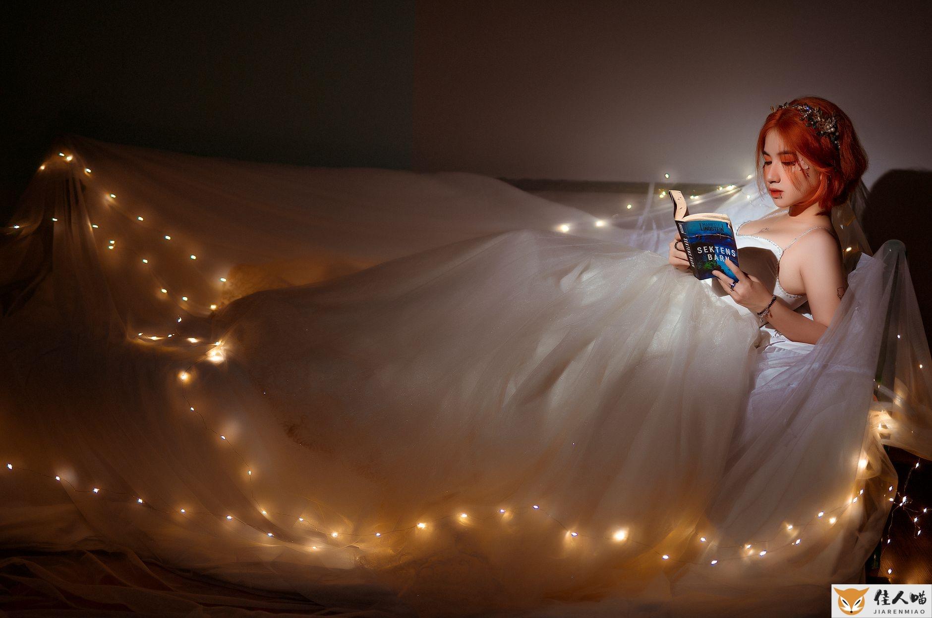 Side view of young ethnic female in bridal dress reading textbook on bed with shiny garland at home